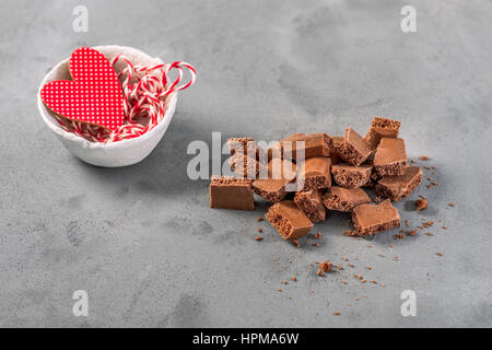 Milk aerated chocolate is on the gray concrete background. Pieces of chocolate are chaotic and sloppy in composition. Around the broken-up chocolate b Stock Photo