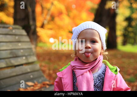 Little girl showes tongue on autumn park background Stock Photo