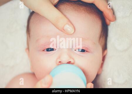 Hungry baby drinking milk. Mother feeding her little boy from bottle. Stock Photo