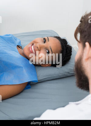 Smiling young woman looking at male doctor while lying on bed in clinic Stock Photo