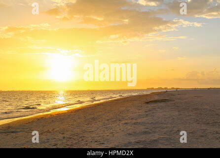 The sun setting in Fort Myers Beach with the skyline and Matanzas Pass Bridge in the distance and the beach in the foreground. Stock Photo