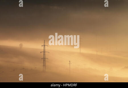 High voltage electric lines in sunny foggy morning in mountais Stock Photo