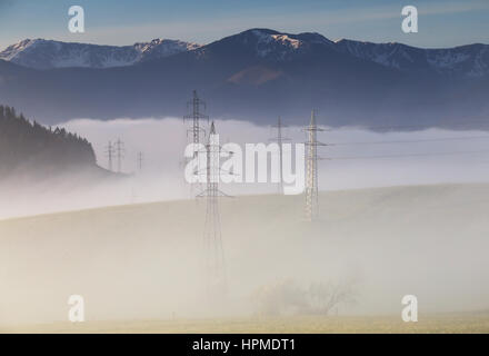 High voltage electric lines in fog in mountais Stock Photo