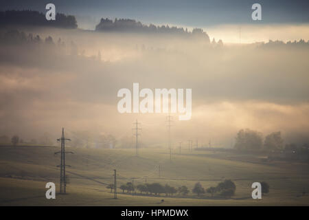 High voltage electric lines in fog on mountain hills Stock Photo
