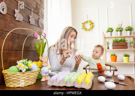 Easter concept. Happy mother and her cute child getting ready for Easter by painting the eggs Stock Photo