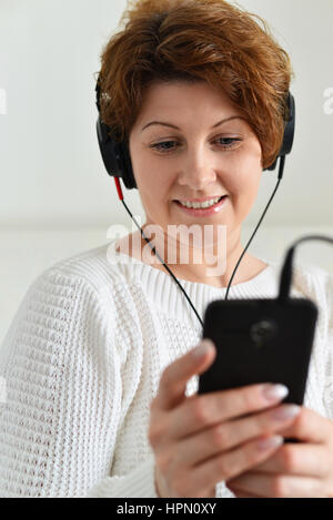 Woman in a headphones looks at smartphone Stock Photo