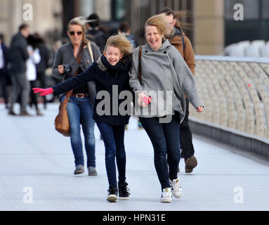 A young girl and a woman laugh as they are caught in a gust of wind as they walk across Millennium Bridge in central London, as flights have been cancelled and commuters were warned they faced delays after Storm Doris reached nearly 90mph on its way to batter Britain. Stock Photo