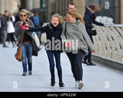 A young girl and a woman laugh as they are caught in a gust of wind as they walk across Millennium Bridge in central London, as flights have been cancelled and commuters were warned they faced delays after Storm Doris reached nearly 90mph on its way to batter Britain. Stock Photo