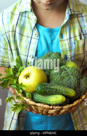 Person (hands) hold basket with organic green vegetables (broccoli, cucumbers, apple and parsley) - healthy organic detox diet vegan vegetarian raw ea Stock Photo