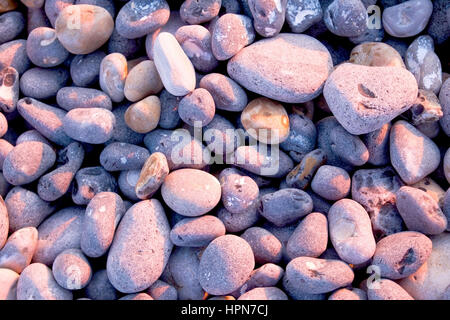 about 50 grey pebbles on beach at sunset, pink glow from the sunset on some of the pebbels, soft shadows, shape and form, overhead view point. Stock Photo