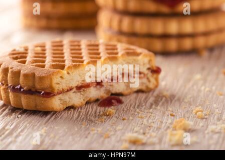 Horizontal photo of several stacks of golden biscuits. Biscuits are with red berry homemade marmalade and one is tasted. Biscuits are placed on light  Stock Photo