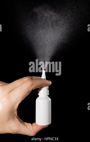 Nasal drug spraying in hand on black background