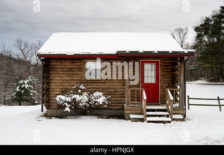 Small log cabin on snowy winter day with steps leading up to red painted door. Stock Photo