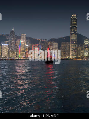 Old traditional Chinese ship with tourists sailing in the Victoria Harbour at night with the skyscrapers and the Hong Kong skyline. China. Stock Photo