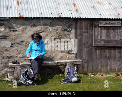 Lone Woman Sat on Bench Reading Comments Book at Dalnashallag Bothy in Glen Banchor on the East Highland Way in the Scottish Highlands, Scotland, UK. Stock Photo