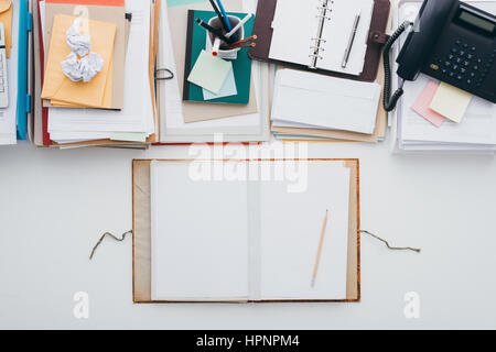 Messy full desktop opposing a tidy clean desktop, piles of paperwork on top and an open folder with blank sheets at bottom Stock Photo