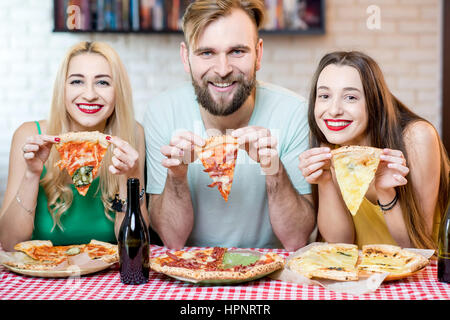 Portrait of young funny friends dressed casually in colorful t-shirts holding slice of pizza at home Stock Photo