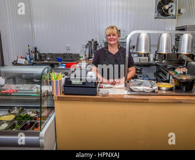 Tje lady owner of a small cafe standing behind the counter in the cafe. Stock Photo
