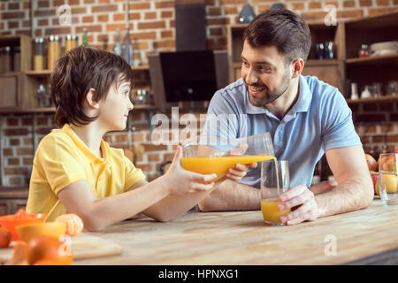 father looking at little son pouring fresh juice in glass Stock Photo