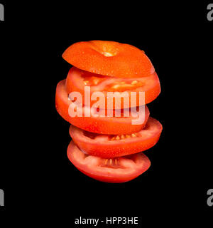 Flying tomato. Sliced red tomato isolated on black background. Levity vegetable floating in the air. Stock Photo