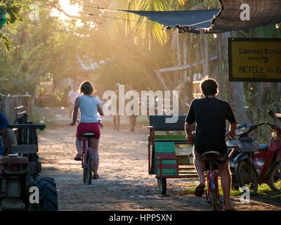 Man and woman riding bicycle in sunset light on small asian road street Stock Photo