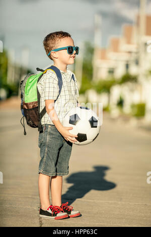 Caucasian little boy standing on the road and holding his soccer ball under his  hands at the day time Stock Photo