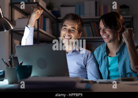 Happy successful winning couple at home with fists raised, they are networking and receiving good news on their laptop Stock Photo