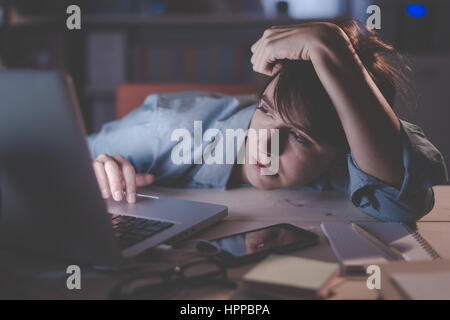 Sleepy exhausted woman working at office desk with her laptop, her eyes are closing and she is about to fall asleep, sleep deprivation and overtime wo Stock Photo
