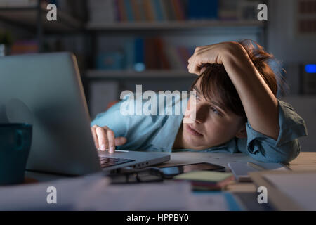 Sleepy exhausted woman working at office desk with her laptop, her eyes are closing and she is about to fall asleep, sleep deprivation and overtime wo Stock Photo