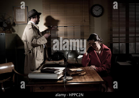 Confident detective standing in his office interviewing a young sad woman. Stock Photo