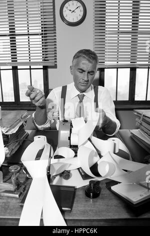 Confused pensive accountant checking very long bills on cash register tape, 1950s style office. Stock Photo