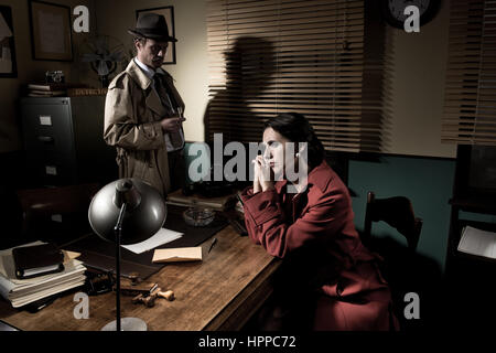 Detective interviewing a young sad woman in his office, film noir scene. Stock Photo