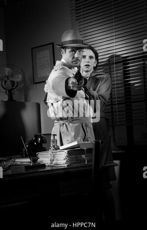Brave detective pointing a gun and young scared woman hiding behind him, 1950s film noir style. Stock Photo