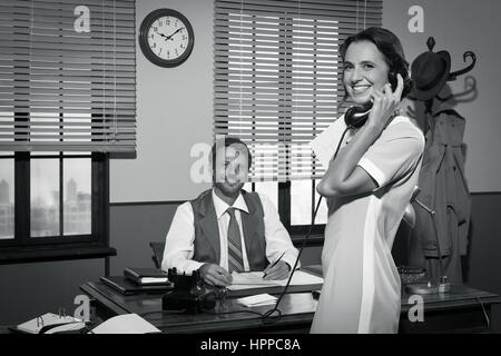 Young 1950s secretary answering phone calls in director's office and smiling. Stock Photo