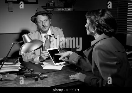 Woman touching detective's tablet sitting at his office desk. Stock Photo