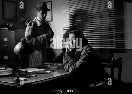 Detective interviewing a young sad woman in his office, film noir scene. Stock Photo