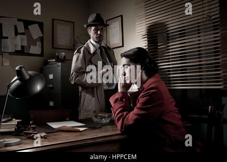 Detective interviewing a young sad woman in his office, film noir scene. Stock Photo