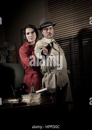 Brave detective pointing a gun and young scared woman hiding behind him, 1950s film noir style. Stock Photo