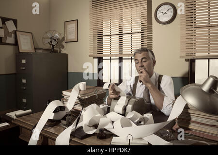 1950s accountant checking calculations in his office with hand on chin. Stock Photo