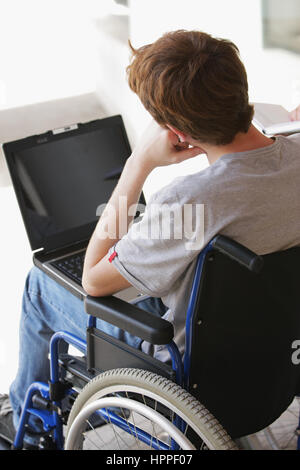 Disabled young man sitting in wheelchair using laptop Stock Photo