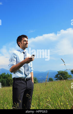 Businessman using smart phone in the meadow on a sunny day Stock Photo