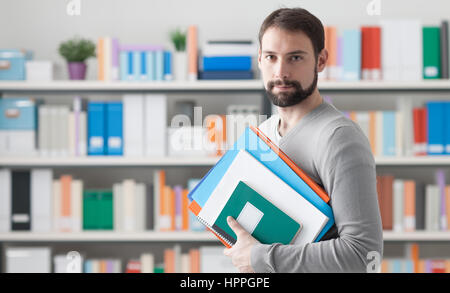 Man holding files and folders and smiling at camera, office shelves with books and files on background Stock Photo