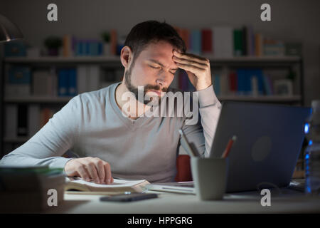 Young man working at office desk late at night and touching his forehead, he is having an headache, stress and overwork concept Stock Photo