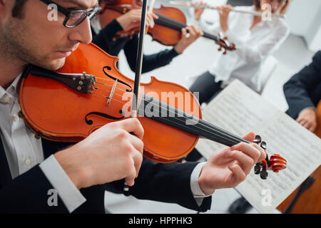 Confident violinist playing his instrument and reading a music sheet, classical music symphony orchestra performing on background Stock Photo