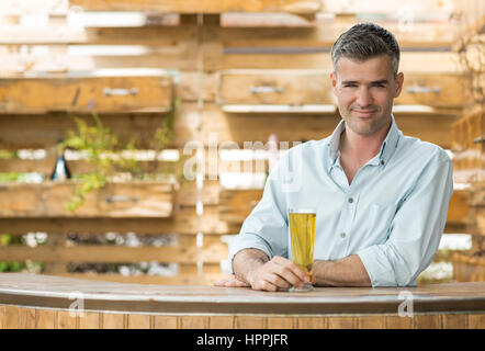 Smiling man having a beer in a rustic pub outdoor, he is leaning on the counter Stock Photo