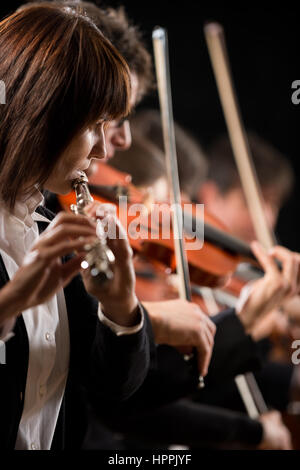 Professional female flutist in concert with symphony orchestra players on background. Stock Photo