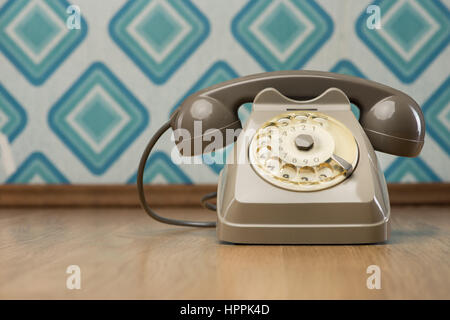 Vintage gray telephone on hardwood floor, diamond light blue retro wallpaper on background. Stock Photo