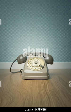 Gray vintage phone on hardwood floor and dotted light blue wallpaper on background. Stock Photo