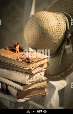 Pile of old books and straw hat with ribbon on a chair. Stock Photo