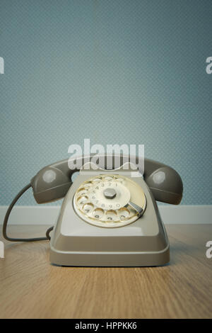 Gray vintage phone on hardwood floor and dotted light blue wallpaper on background. Stock Photo